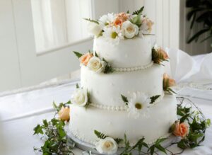 Home Elegant white wedding cake adorned with fresh roses and daisies, perfect for a romantic celebration.